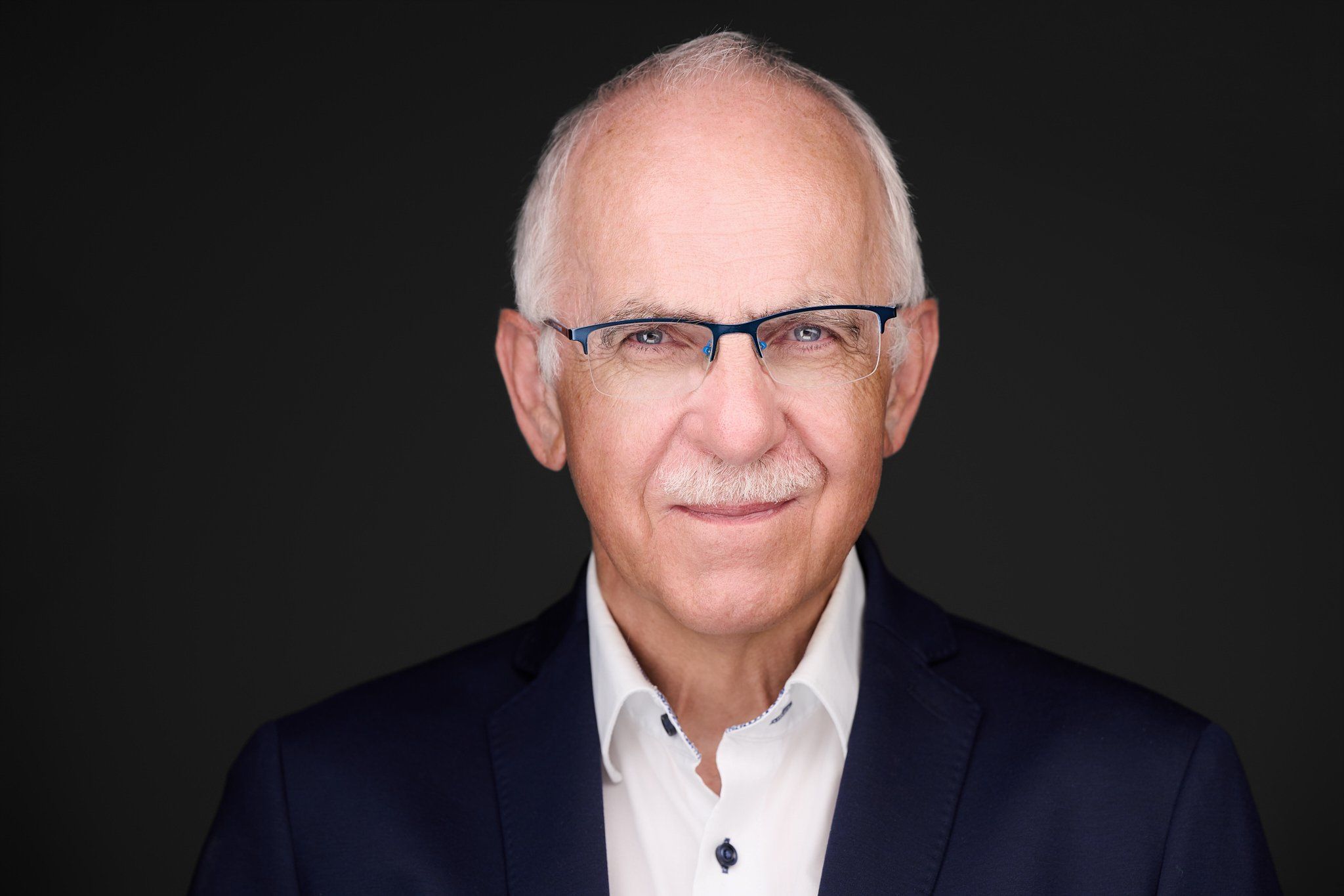 Neuer Headshot von Stefan: Businessportrait mit weißen Haaren, Brille und dunklem Anzug vor schwarzem Hintergrund, fotografiert im Studio in Köln